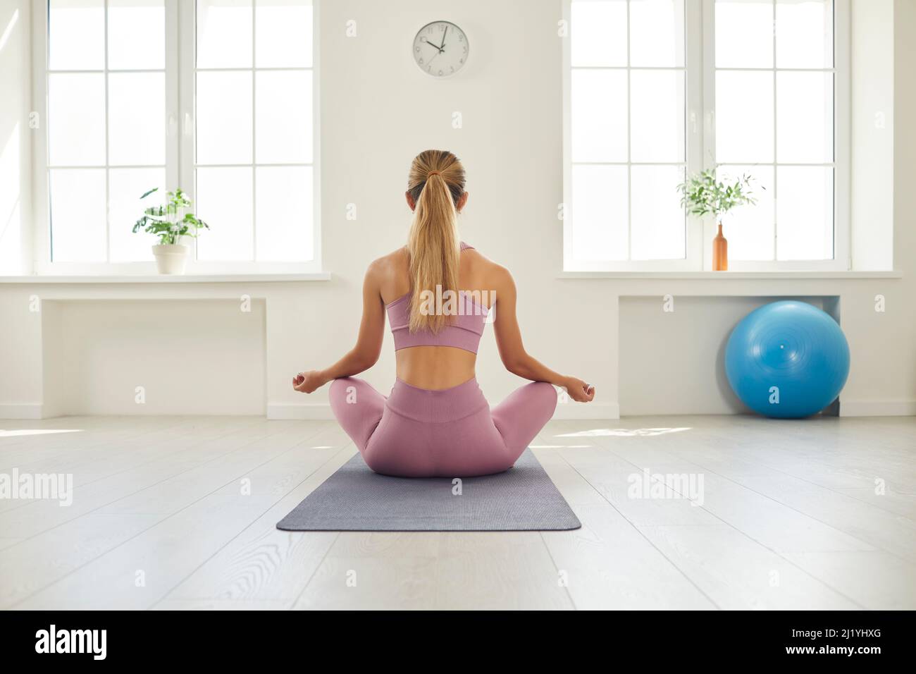 Back view of slender young woman in sportswear sitting in lotus position doing yoga. Stock Photo