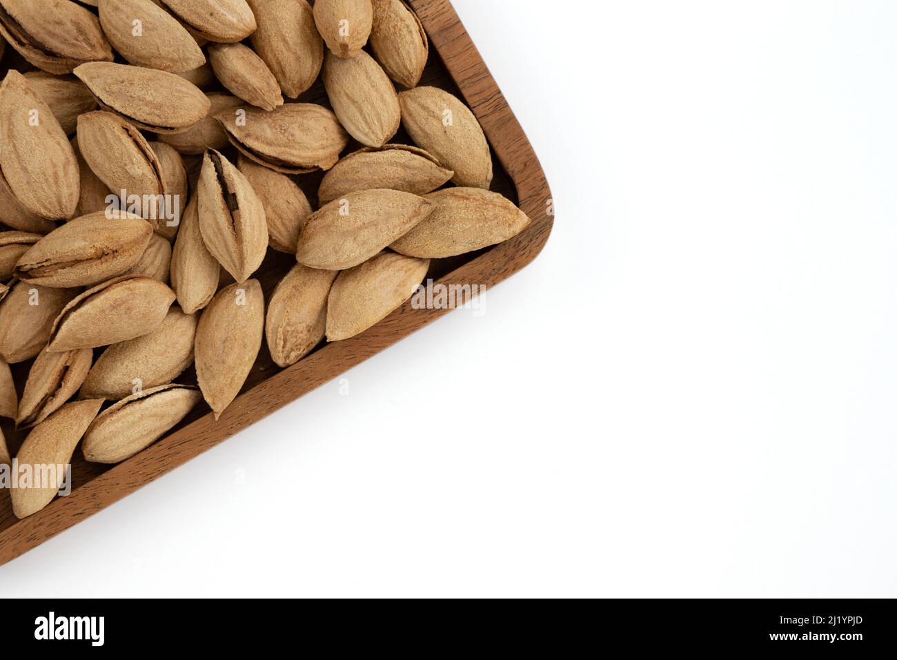 top view of unpeeled almonds drupes in wooden plate isolated on white