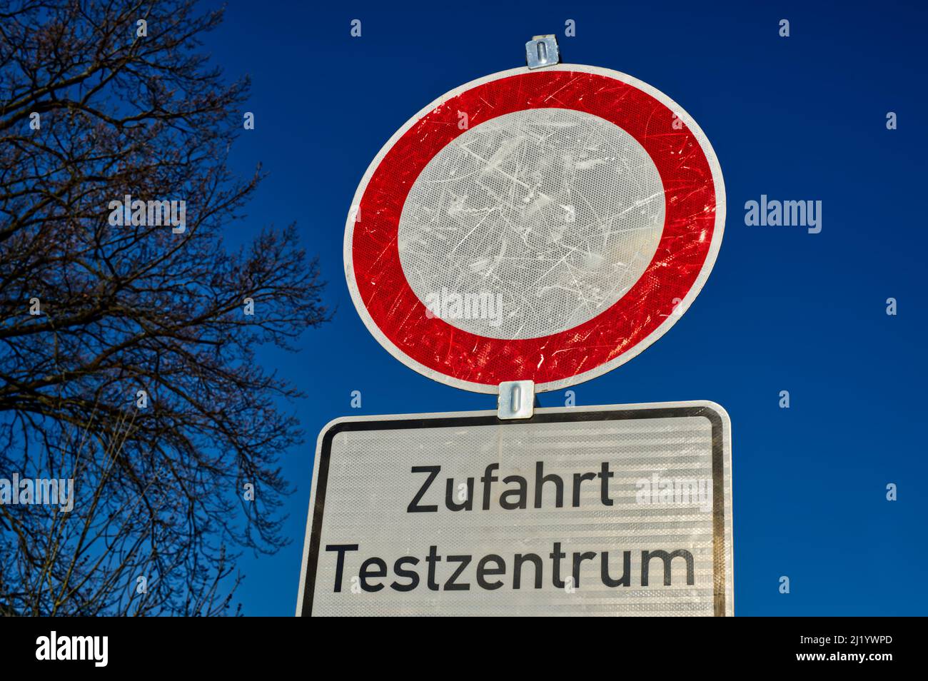 circular red-white road sign and German lettering "Zufahrt Testzentrum" ("driveway to test center") with a few branches in clear blue sky Stock Photo