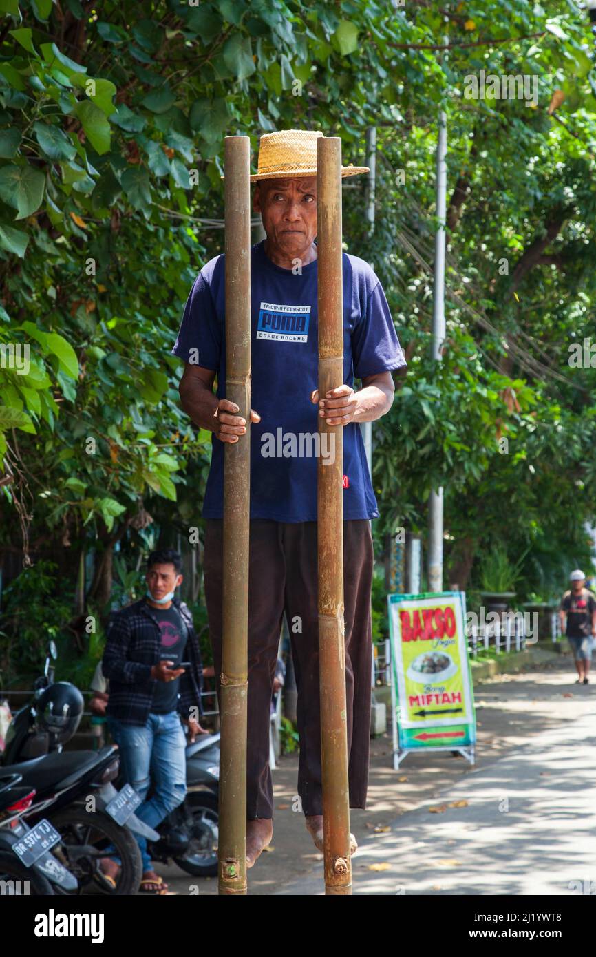 An elderly man performing by walking on stilts on the roadside near in Denpasar Bali, Indonesia. Stock Photo