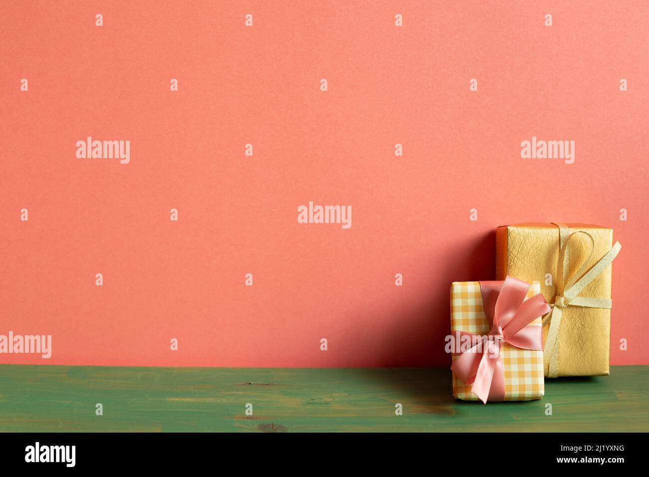 Yellow and gold gift box on green wooden table. pink wall background. copy space Stock Photo