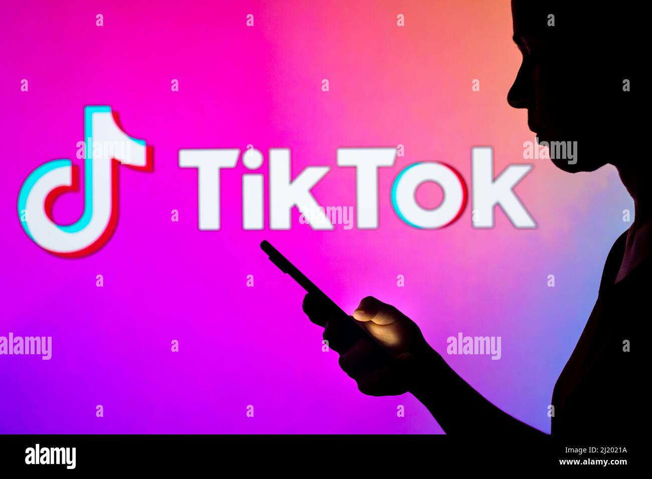 In this photo illustration, a woman's silhouette holds a smartphone with the TikTok logo in the background. Stock Photo