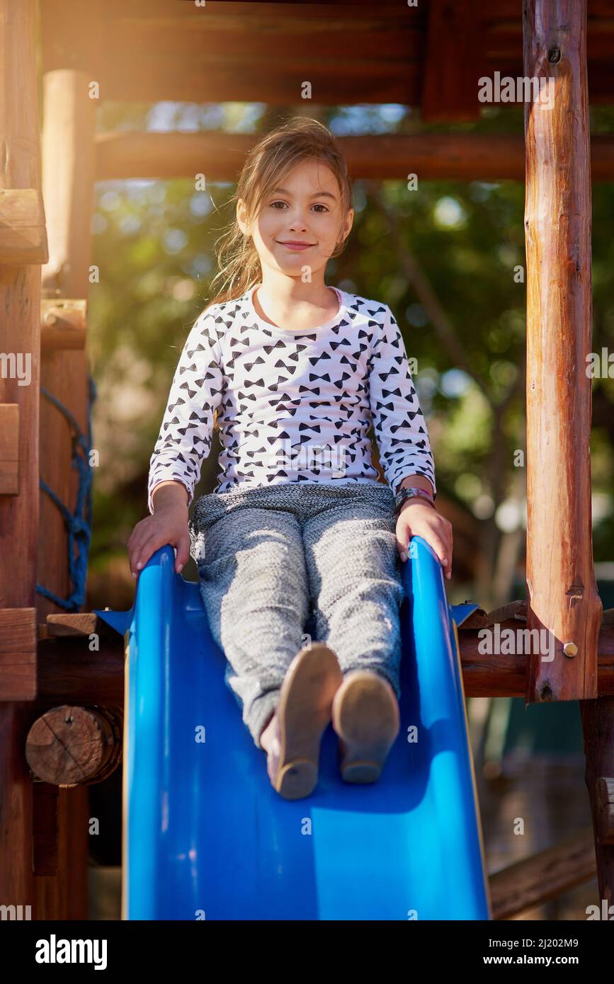 The slide is my favourite at the park. Portrait of a little girl playing on a slide at the park. Stock Photo