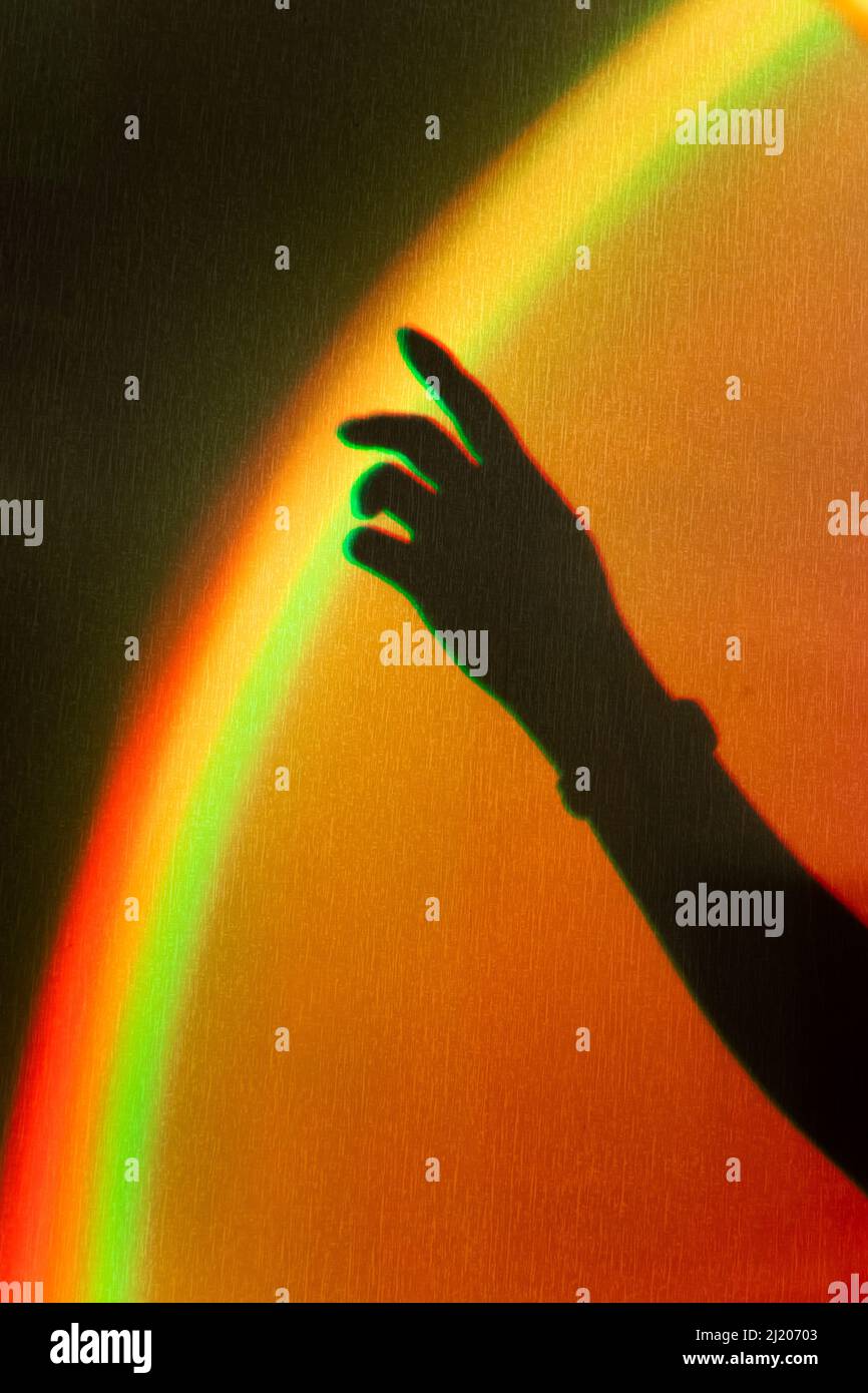 Shadow of womans hand. Rainbow reflection of sunbeam on wall. Hand touches rainbow. Concept of dreams and hopes. Stock Photo