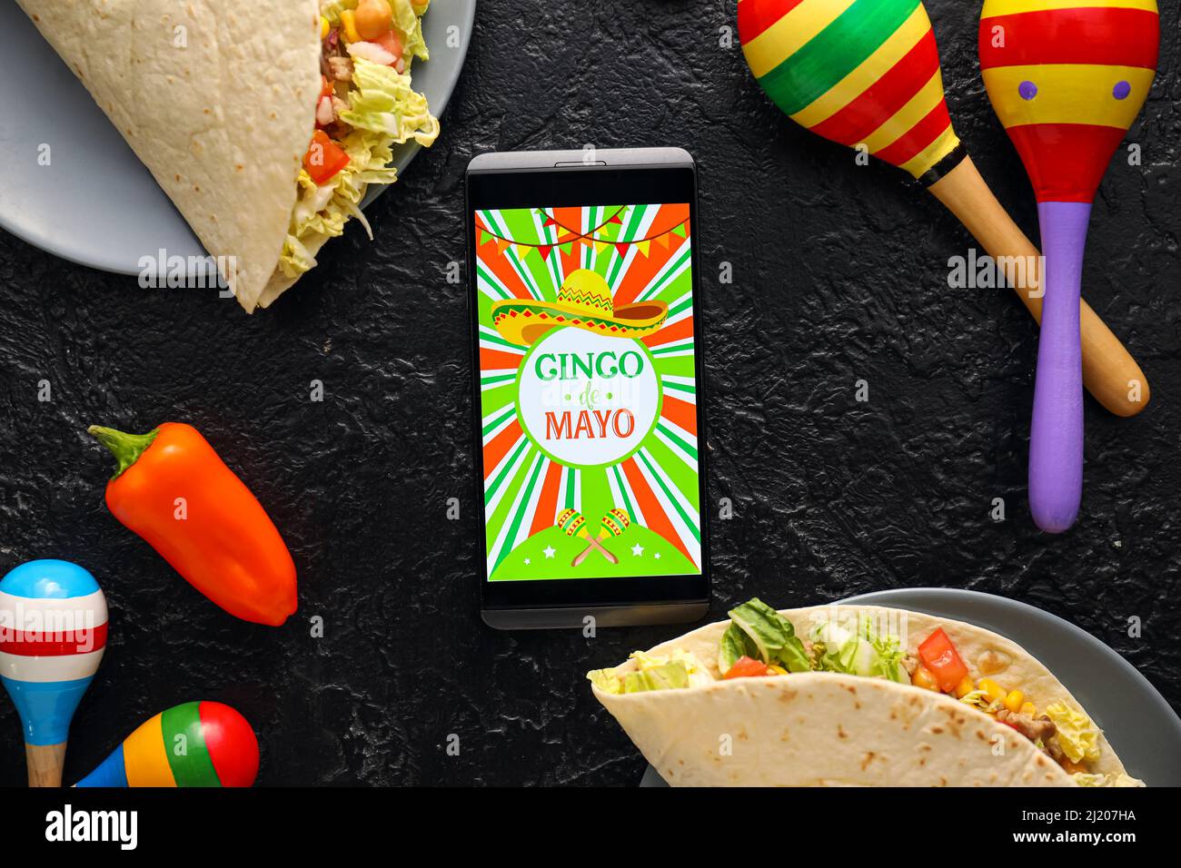 Traditional Mexican tacos, maracas and mobile phone on dark background