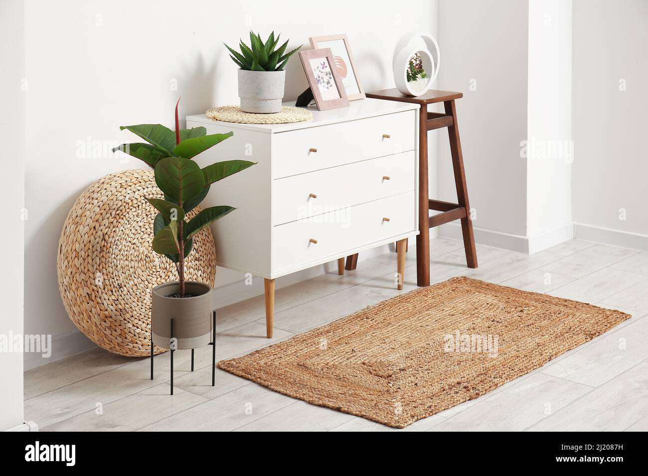 Interior of light room with chest of drawers, houseplants and wicker ...