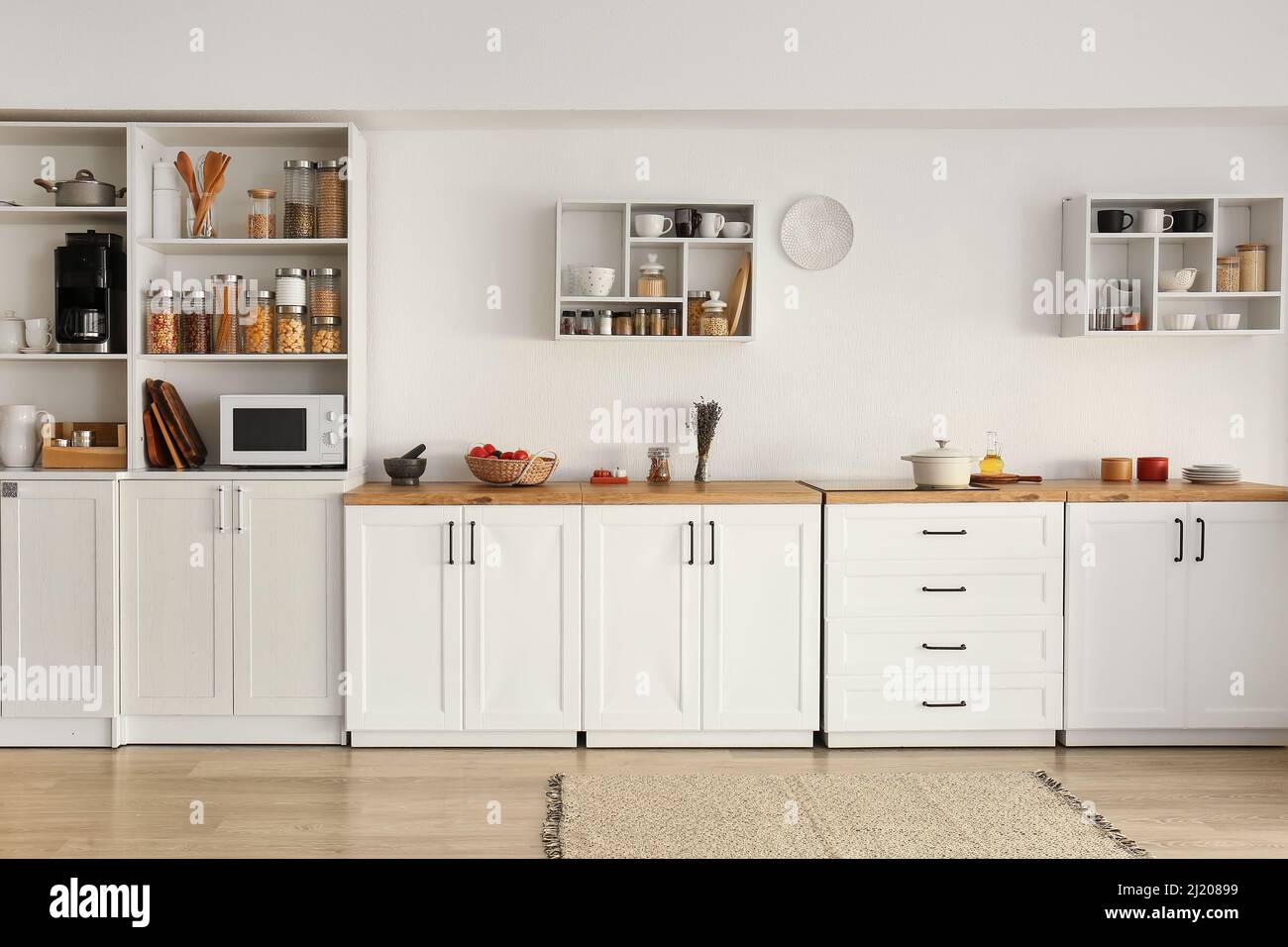 Interior of light modern kitchen with white counters, shelves and food ...