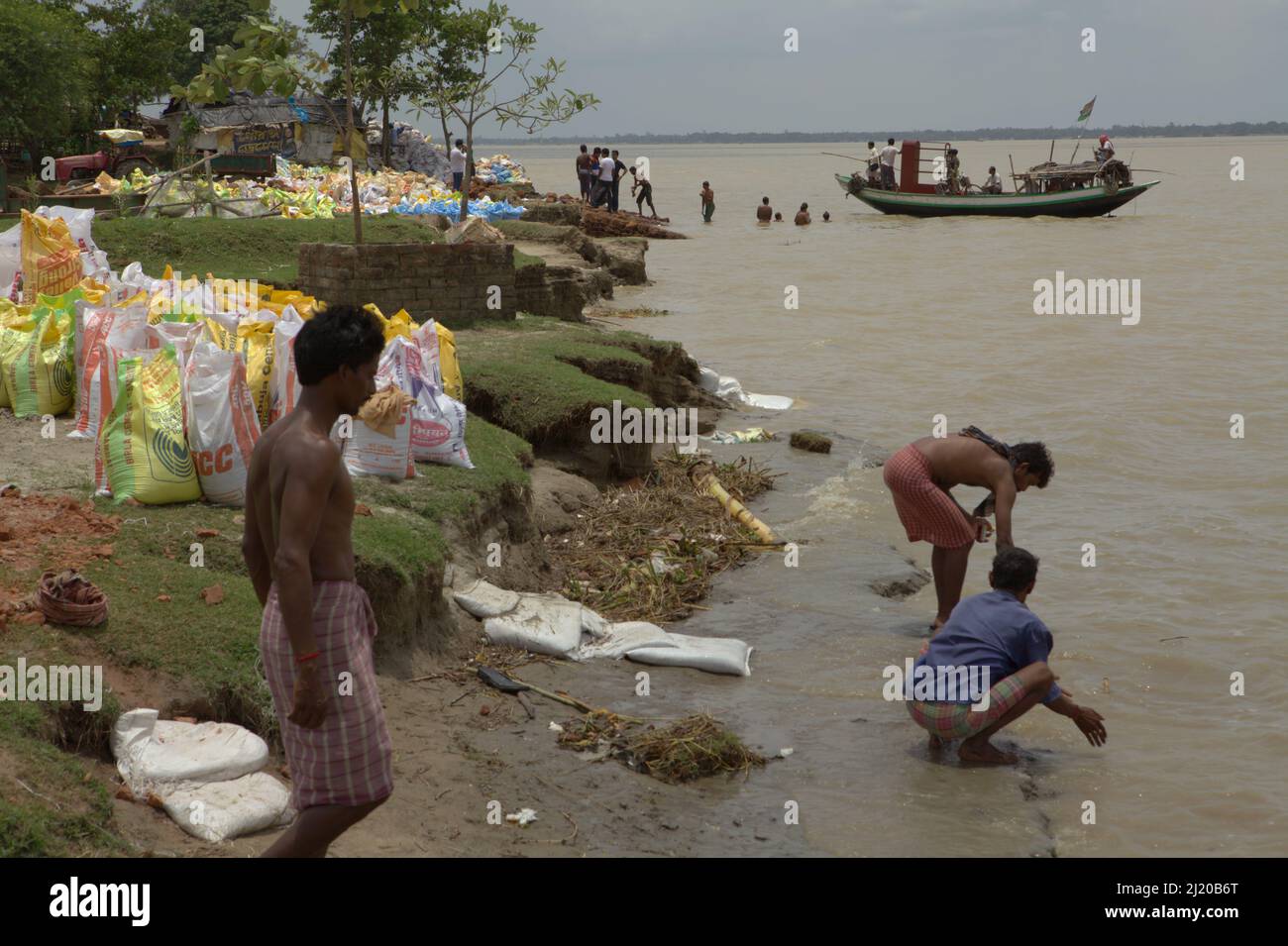 Workers of a river abrasion protection project washing themselves on the bank of Rupnarayan river as a local ferry boat was a about to land in Tamluk, Purba Medinipur, West Bengal, India. Known as Tamralipti in ancient times, Tamluk was the main gate for Nalanda-bound Buddhist pilgrims coming from the sea from Kuang-tung (now Guangzhou, China), a long sail that would need a transit in Srivijaya empire's harbours along the present-day Malacca Strait. 'On the eighth day in the second month in the fourth year of the Hsien Heng period (673 A.D.), I arrived at Tamralipti.' Stock Photo