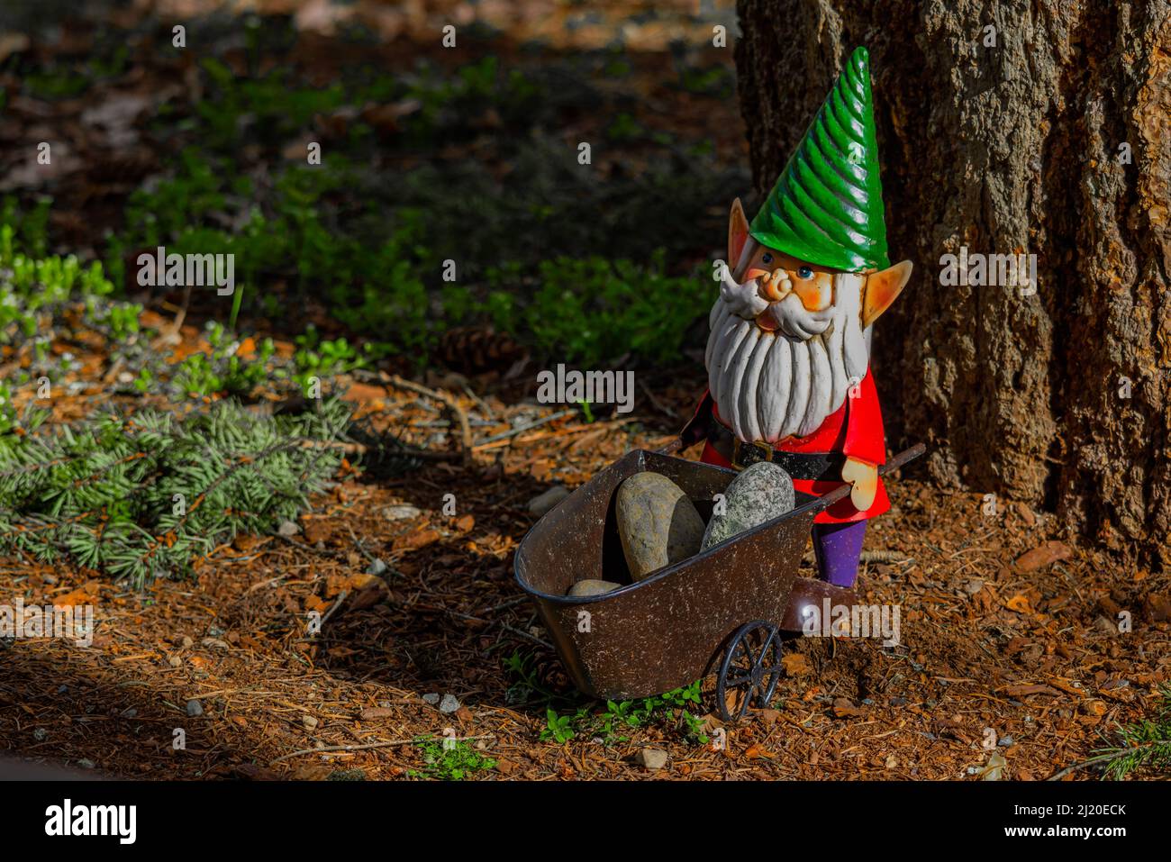 Metal lawn gnome holding pile of rocks in wheelbarrow standing on top