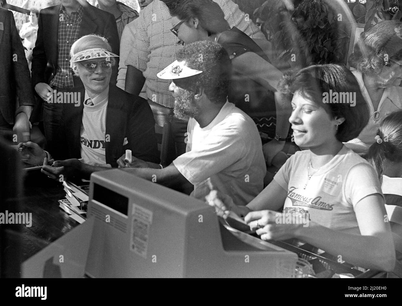 A an event billed as 'Amos and Andy' in the Hollywood outlet for Famous Amos Cookies, Andy Warhol and Wally Amos sign books beside a cash register. Los Angeles, CA., 1979. Stock Photo