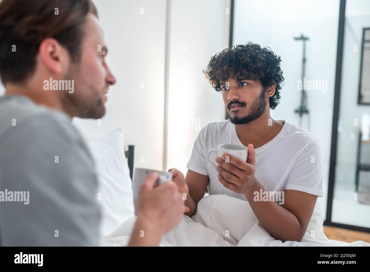 Cute man drinking coffee with his partner in the bedroom Stock Photo