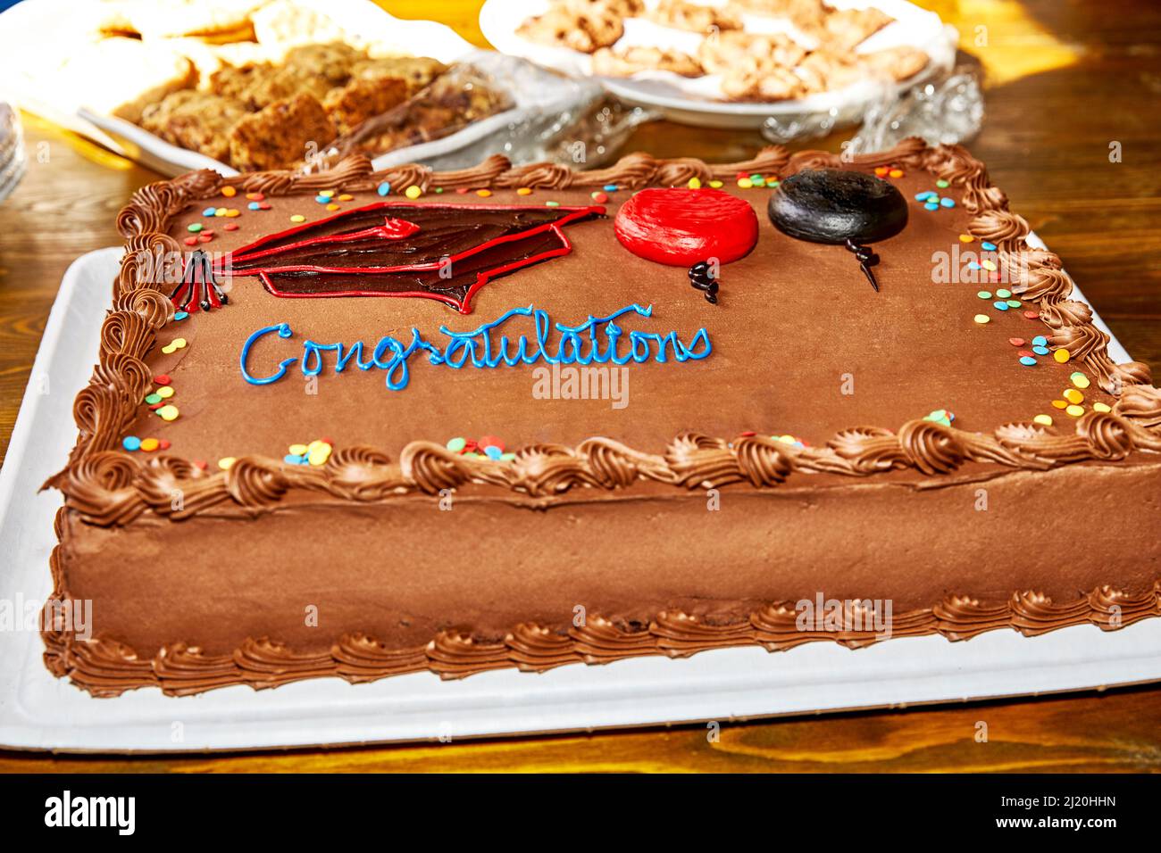 Chocolate graduation cake with decorations and cookies in the background with shallow depth of field Stock Photo