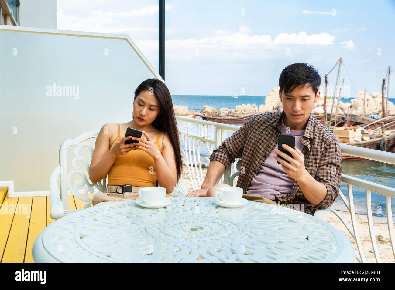 Young couple using cell phones at coastal cafe by the fish Boat pier - stock photo Stock Photo