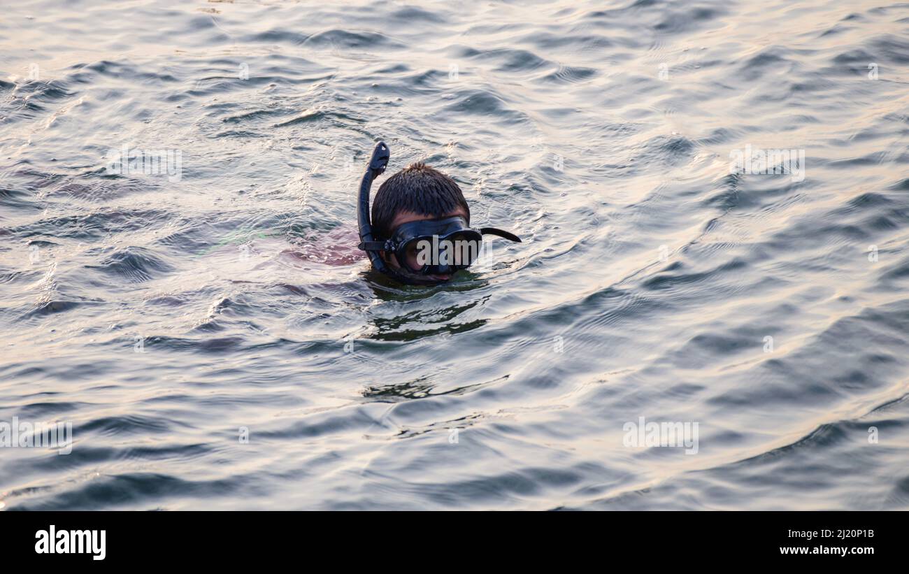 Man wearing goggles and swims in the ocean in the afternoon Stock Photo
