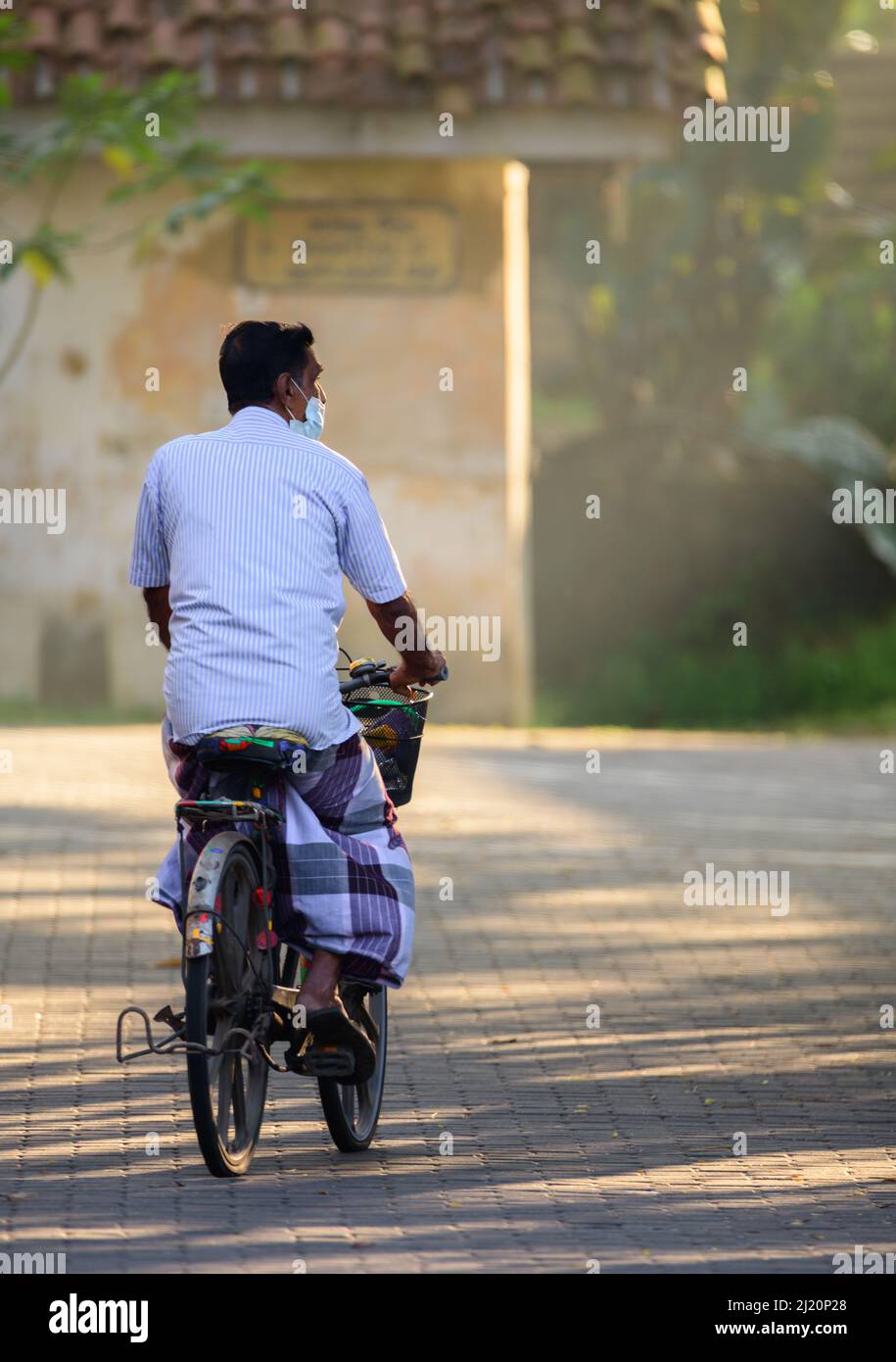 Galle, Sri Lanka - 02 26 2022: Concept of everyday life in Sri Lanka, Elderly ride away in a bicycle, early in the morning, Stock Photo