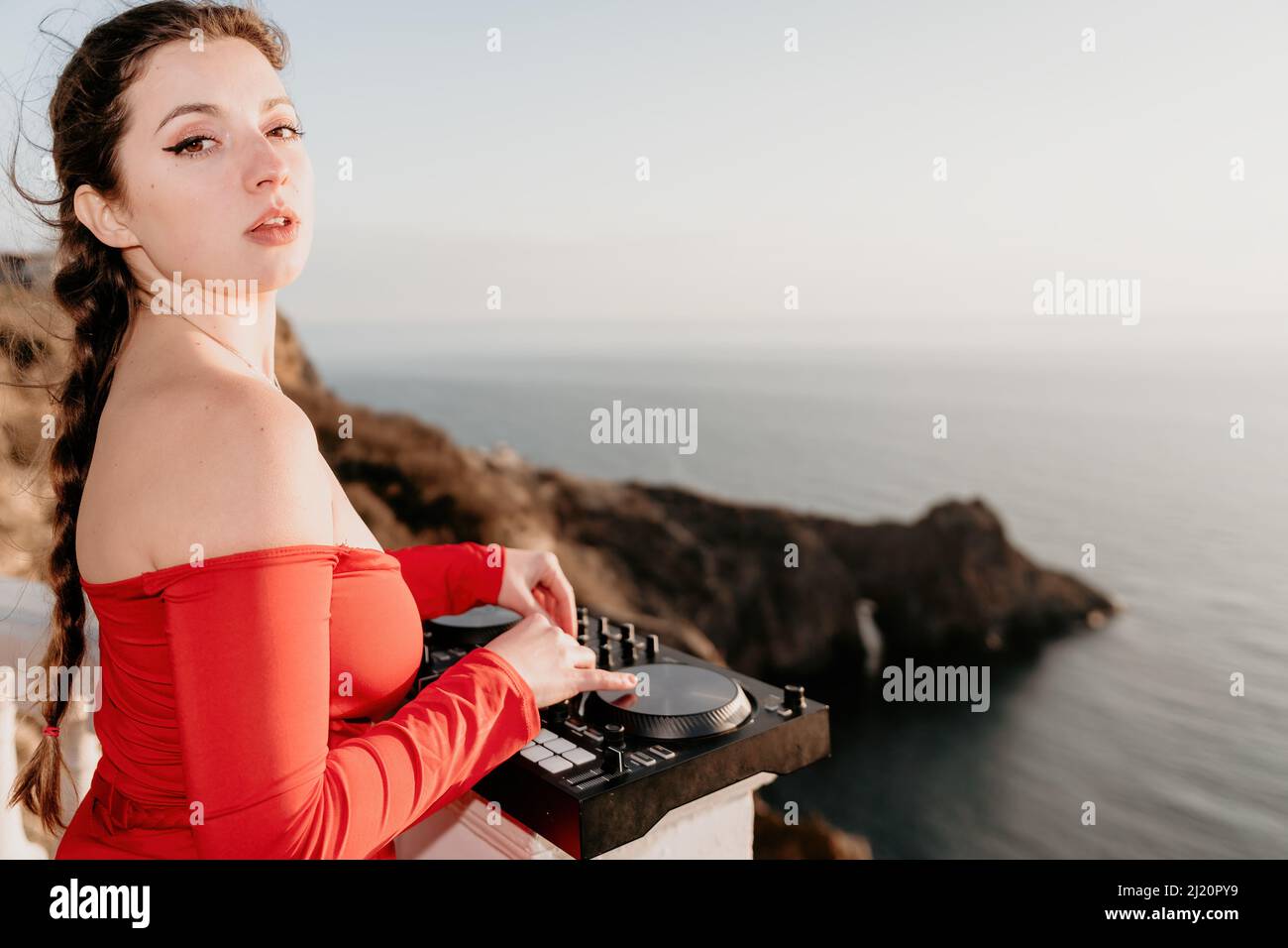 Female Hands of DJ plays music mixing and scratching on evening party with sea background and soft warm sunset. Close-up of a DJ console controlled by Stock Photo