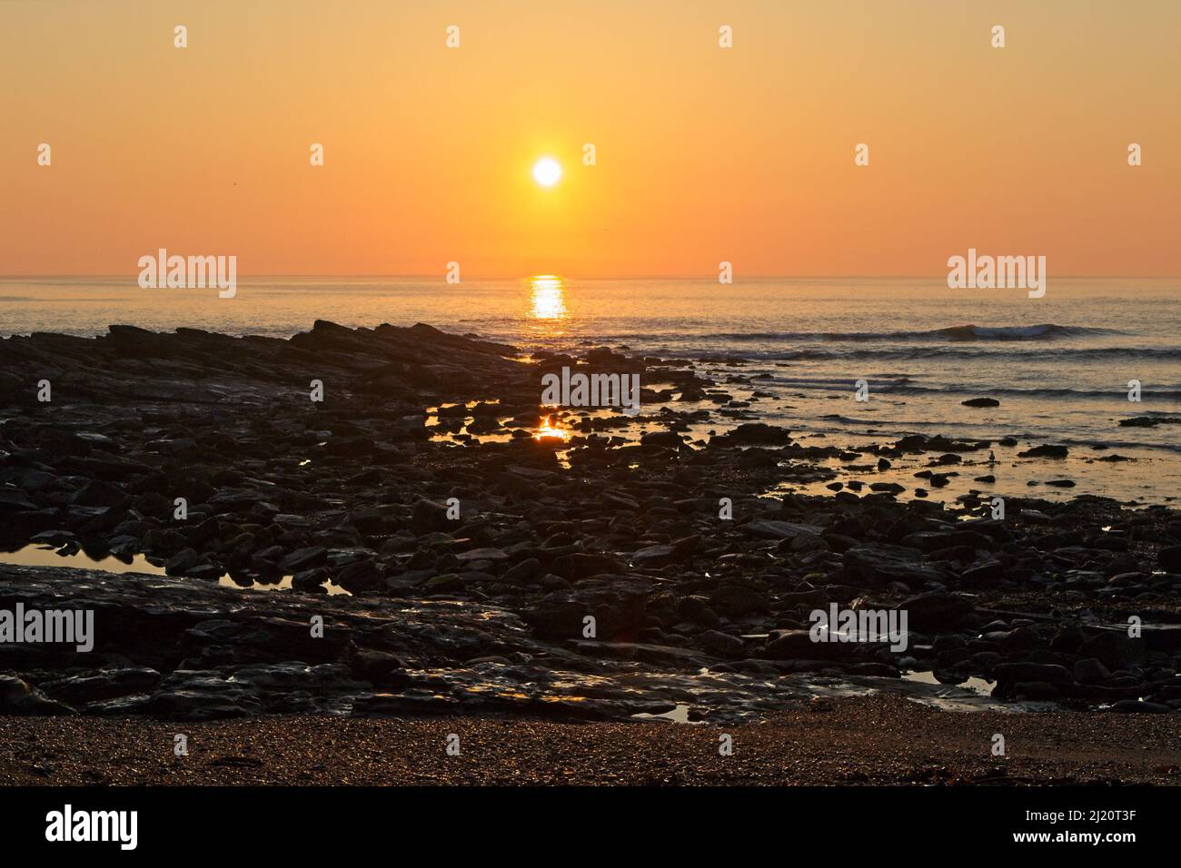Sun rises above the sea at Collywell Bay casting an orange glow in the sky near Seaton Sluice in North Tyneside. Stock Photo