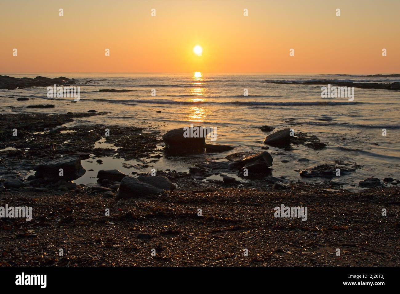 Sun rises above the sea at Collywell Bay casting an orange glow in the sky near Seaton Sluice in North Tyneside. Stock Photo