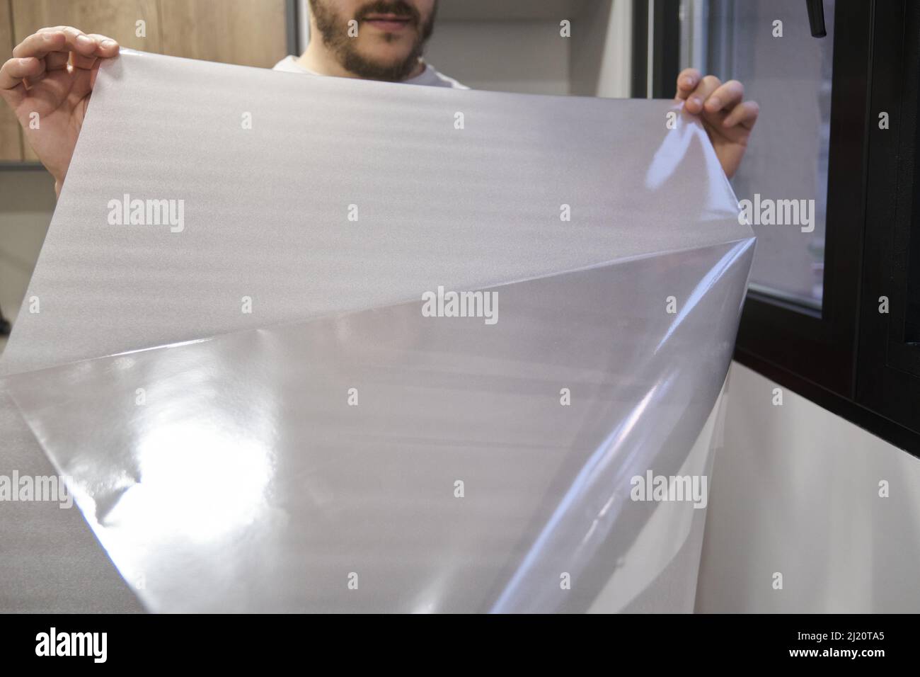 Man taking off the plastic to install frosted window vinyl on the window glass. Stock Photo