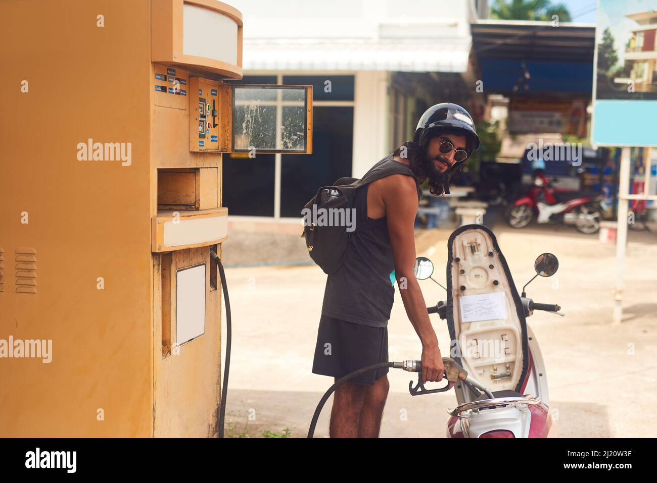 You wont get far without gas. Shot of a young tourist refueling his scooter at a gas station while exploring a foreign city. Stock Photo