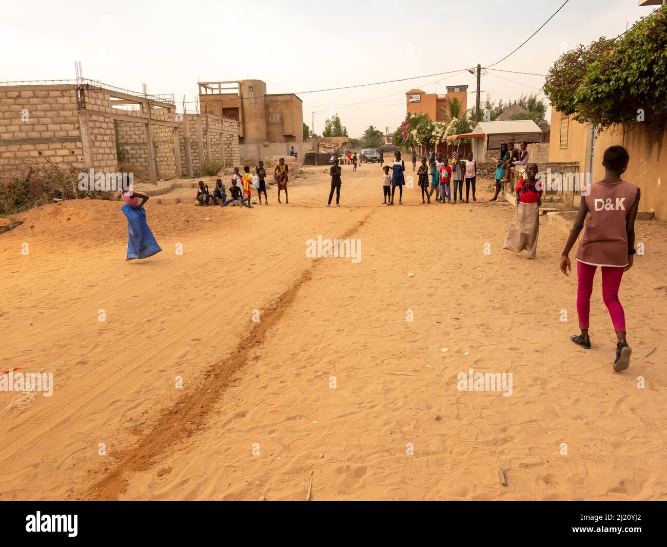 MBOUR, SENEGAL, AFRICA - DECEMBER Circa, 2021. Unidentified young african children doing a sack race in the street. They have to fill the basin with w Stock Photo