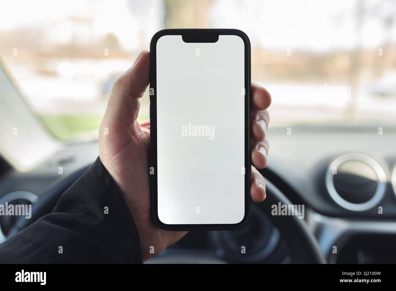 Smartphone with blank white screen in hands of male driver over car steering wheel, selective focus Stock Photo