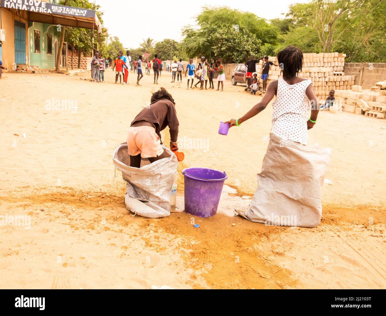 MBOUR, SENEGAL, AFRICA - DECEMBER Circa, 2021. Unidentified young african children doing a sack race in the street. They have to fill the basin with w Stock Photo