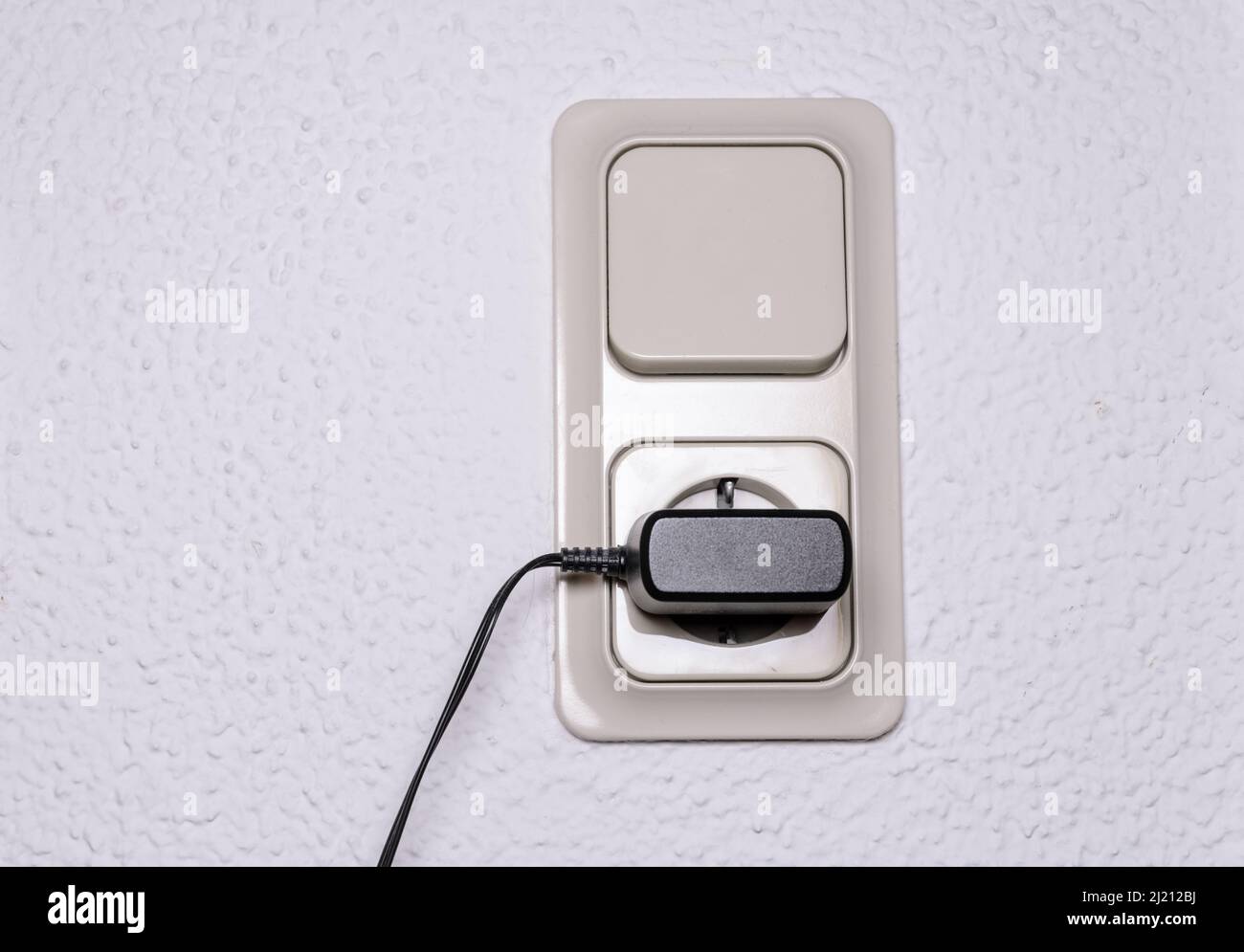 Modern light switch and german power outlet or socket on white wall indoors with black phone charger plugged in, Germany, Europe Stock Photo
