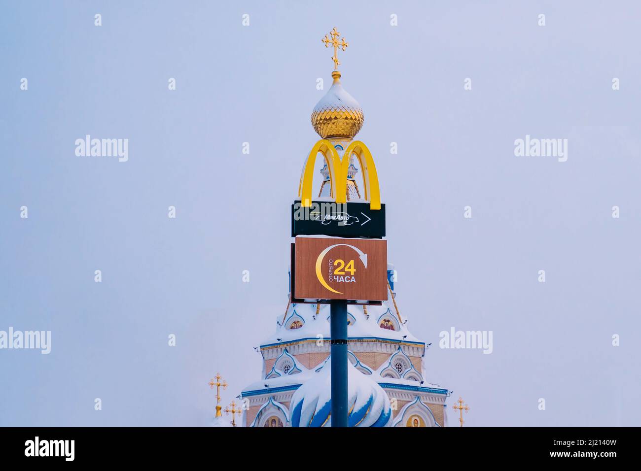 Izhevsk, Russia. March 01, 2022. McDonald's symbol in the background of the Russian Orthodox Church. Confrontation between Western business and the Ru Stock Photo