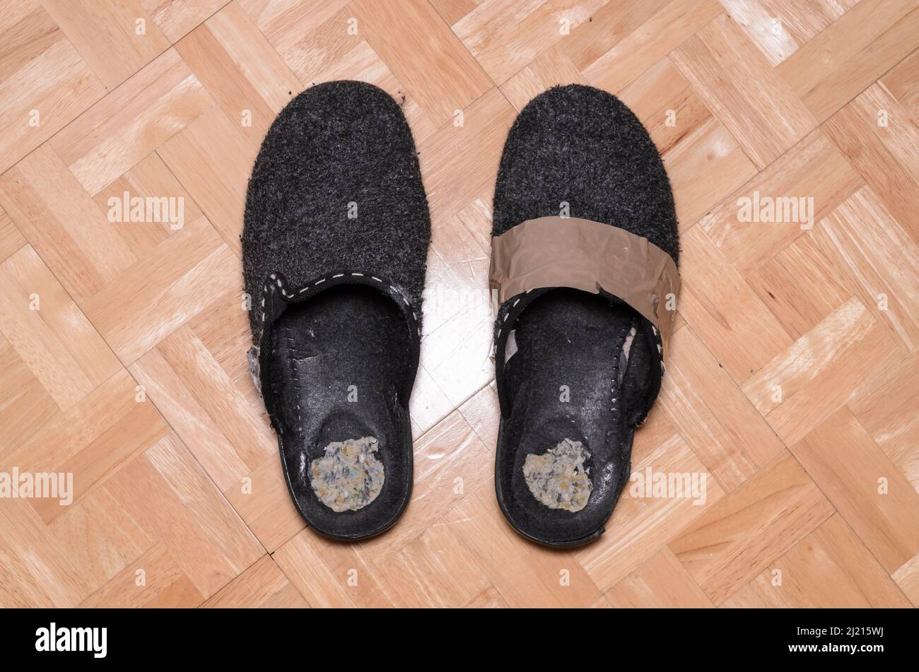 Old pair of worn slippers on wooden floor, reinforced with duct tape