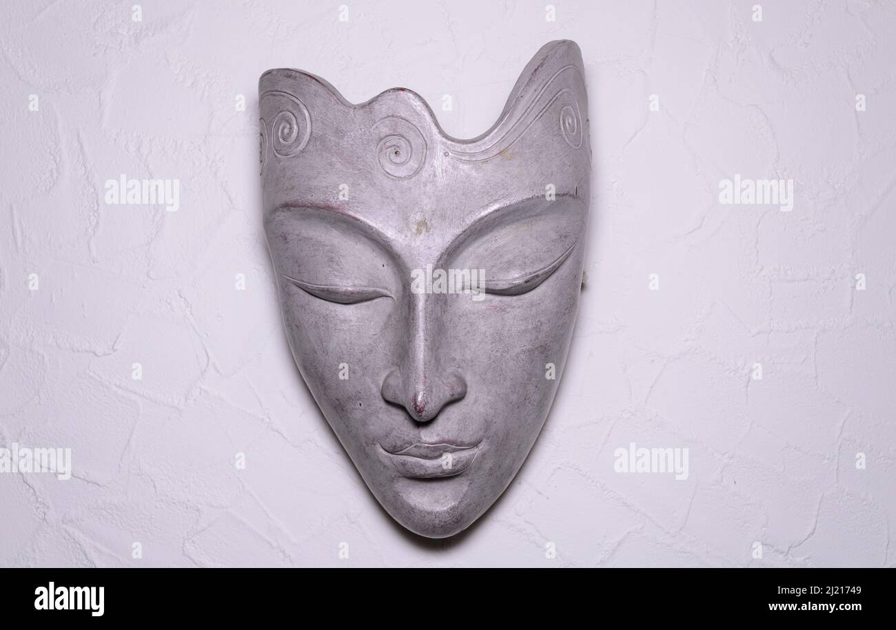 Decorative asian or oriental face mask made of grey stone on a white wall, front view Stock Photo