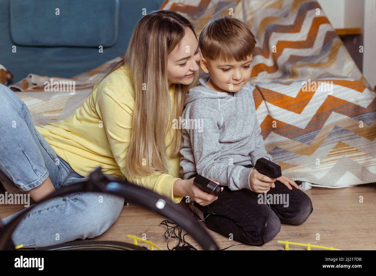 Mom and little son play racing on the carpet at home, have fun and hug. Single mother raises her son by playing cars Stock Photo