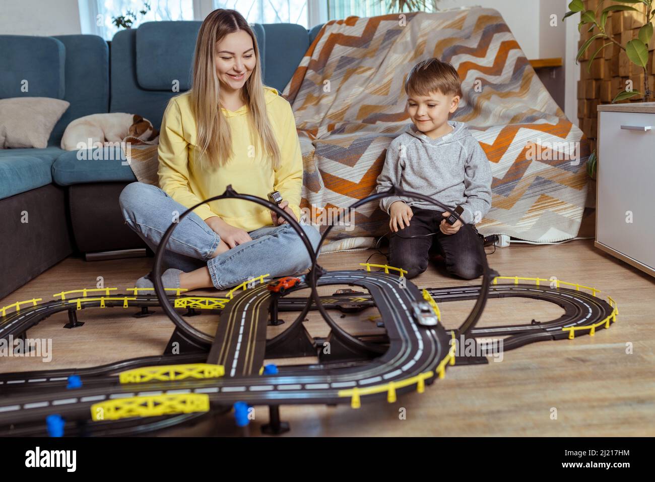Mom and little son play racing on the carpet at home, have fun and hug. Single mother raises her son by playing cars Stock Photo