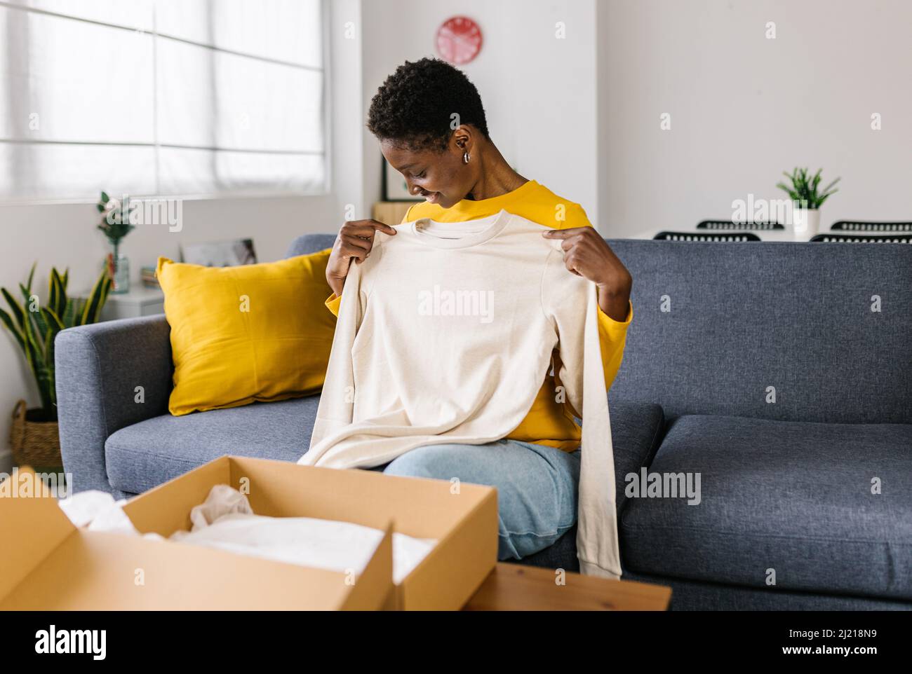 Woman opening a parcel box with a clothing item from an online purchase. Stock Photo