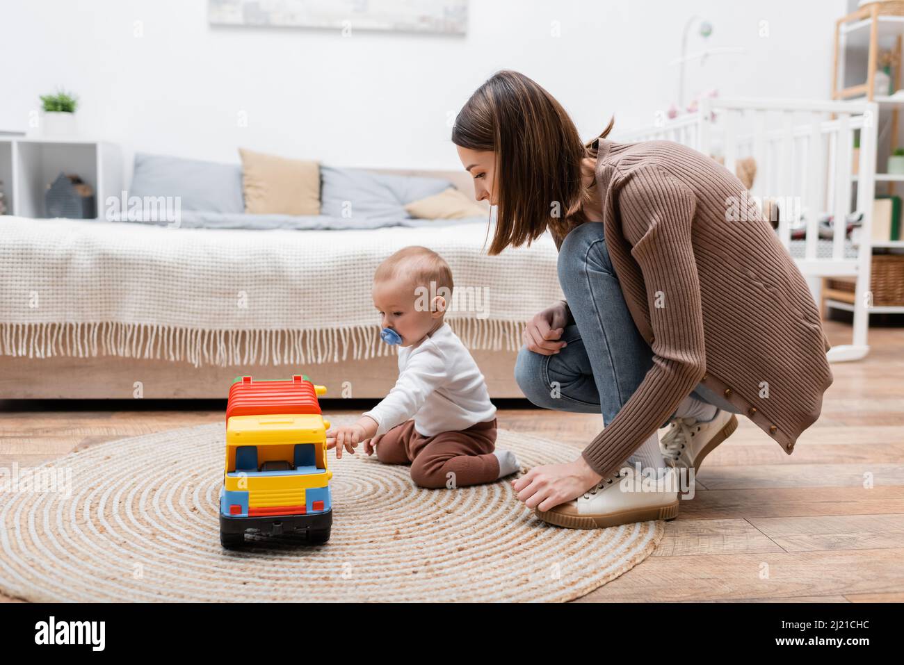 Parent looking at baby son with pacifier playing with toy car at home