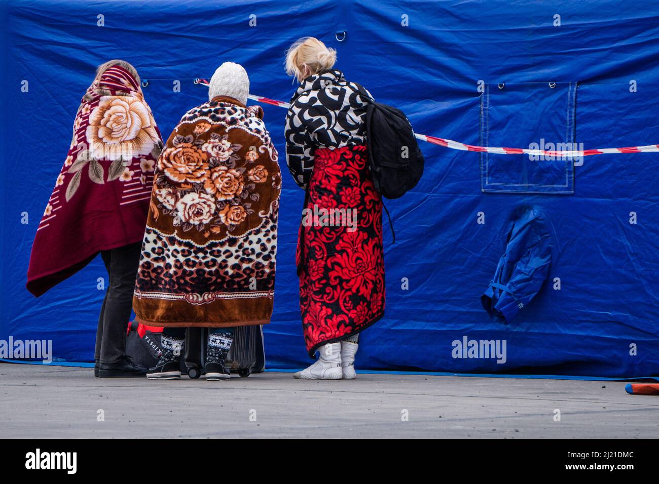 Three Ukrainian women huddle up, covered in warm blankets, waiting to