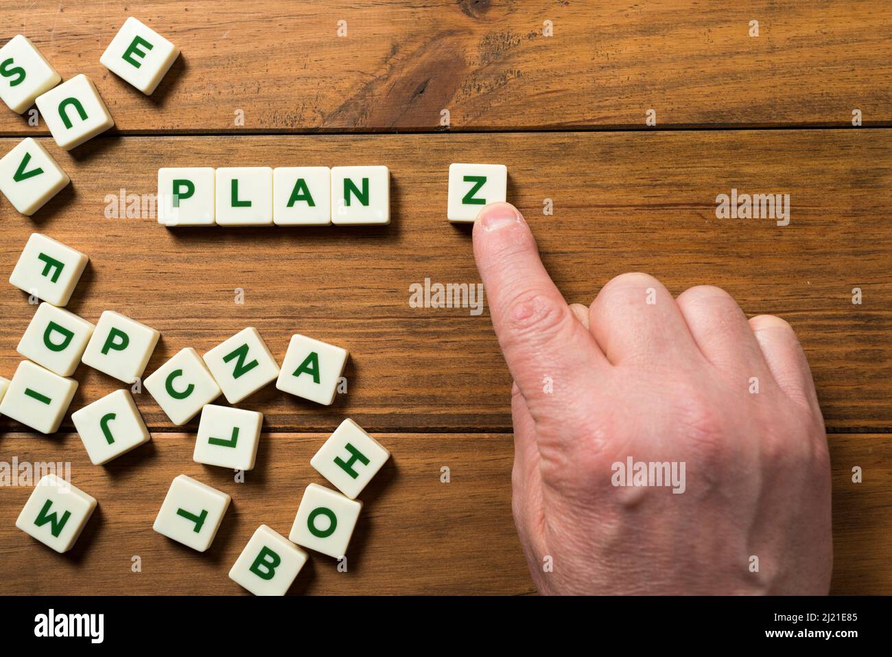A hand places a piece with the letter Z next to the word PLAN; around it other letters appear in disarray. Concept of planning for the future, resilie Stock Photo
