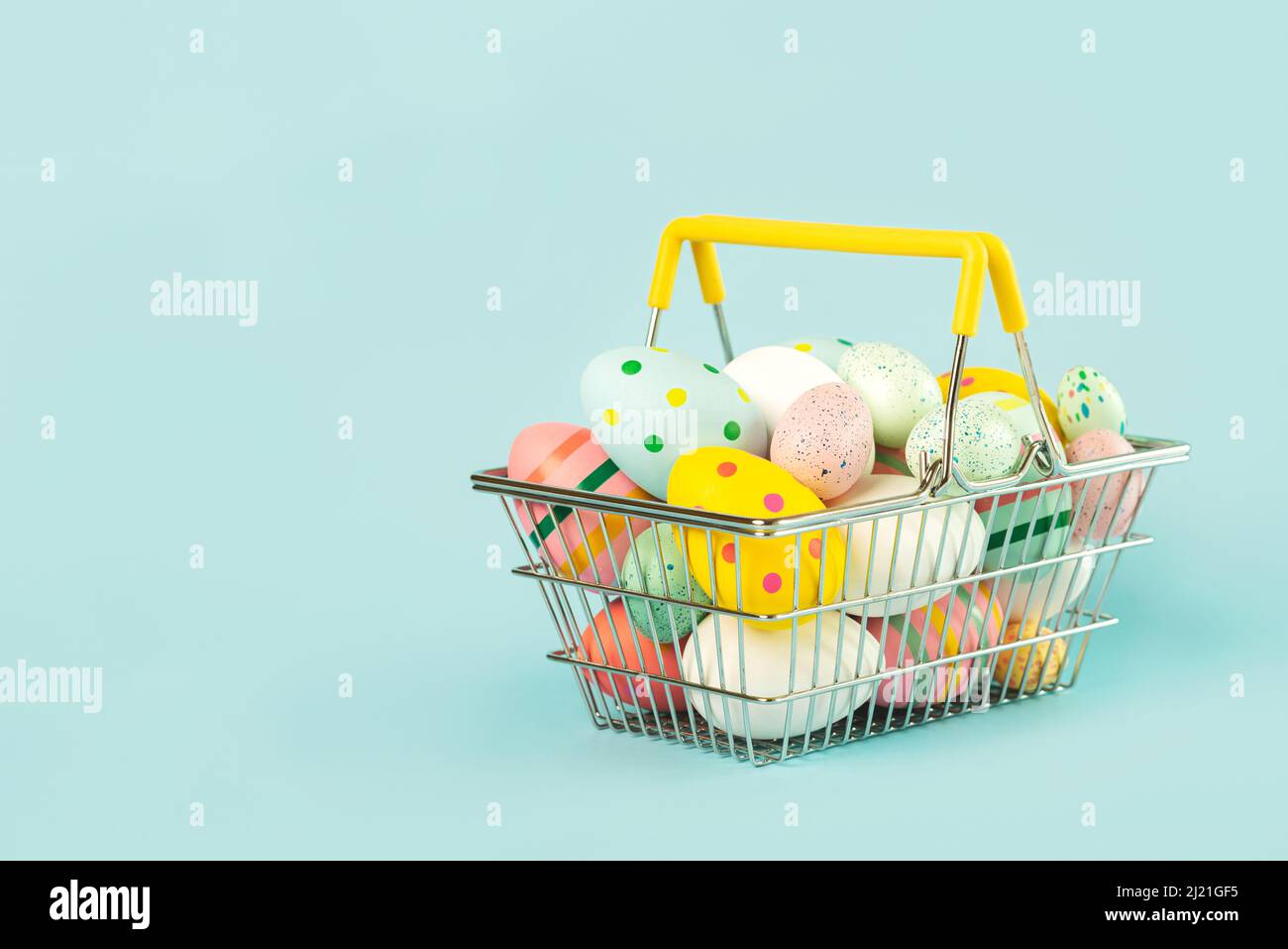 Happy Easter. Colored easter painted eggs in a shopping basket with copy space over blue background Stock Photo