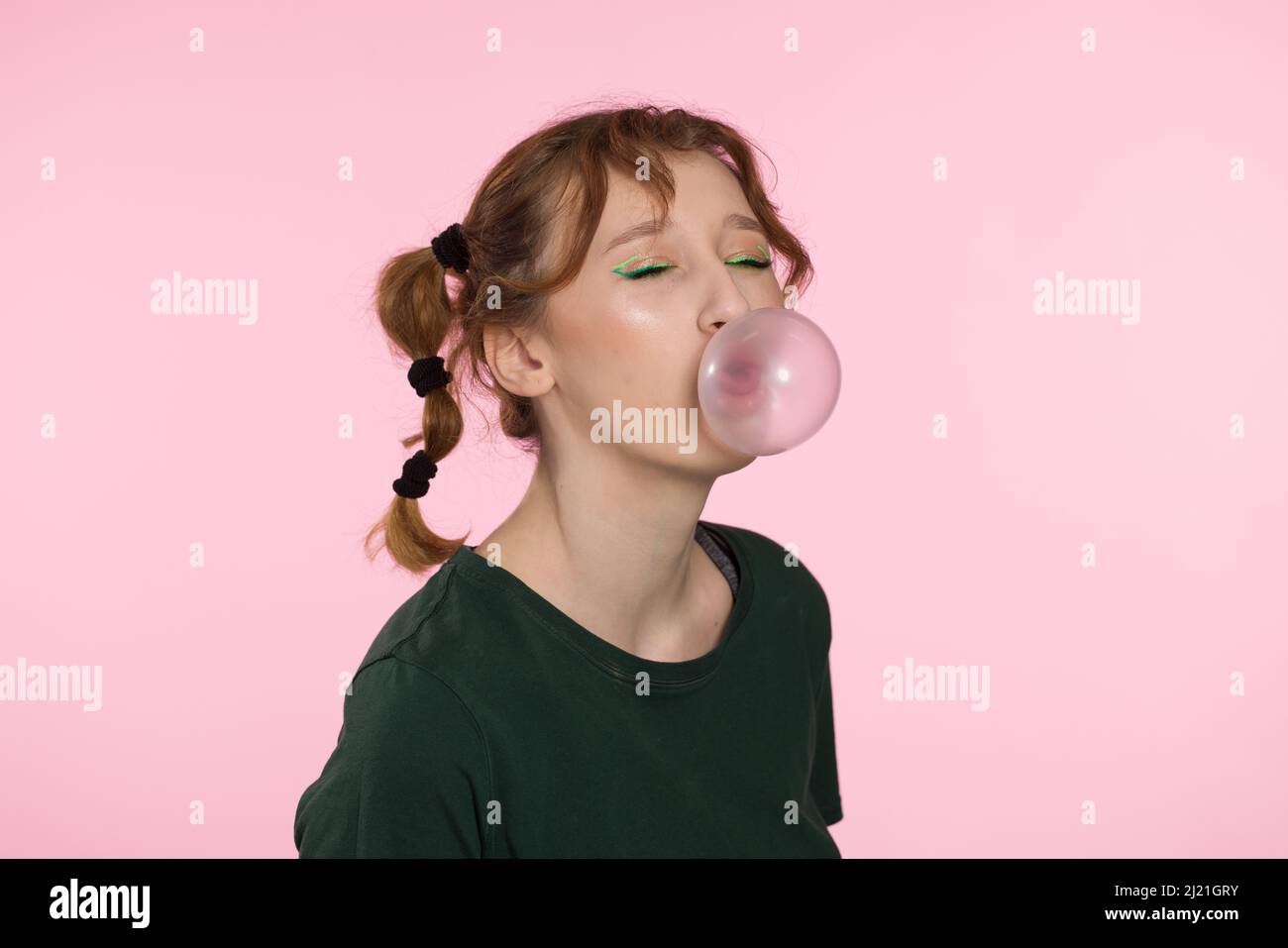 Bubble from chewing gum. Young teenage girl blowing pink bubble gum. Girl blowing large bubble isolated pink color background Stock Photo