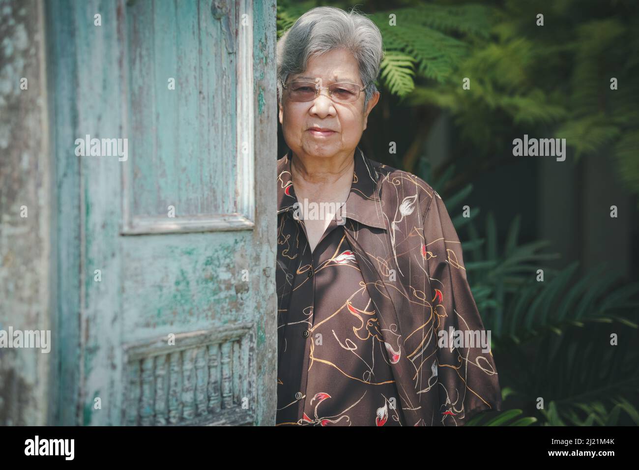 old elderly elder woman standing near old blue wooden door Stock Photo