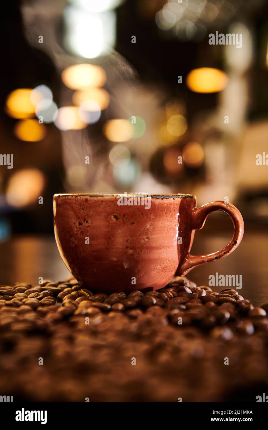 A hot modern cup of coffee on top of a pile of coffee beans in a well lit trendy interior Stock Photo