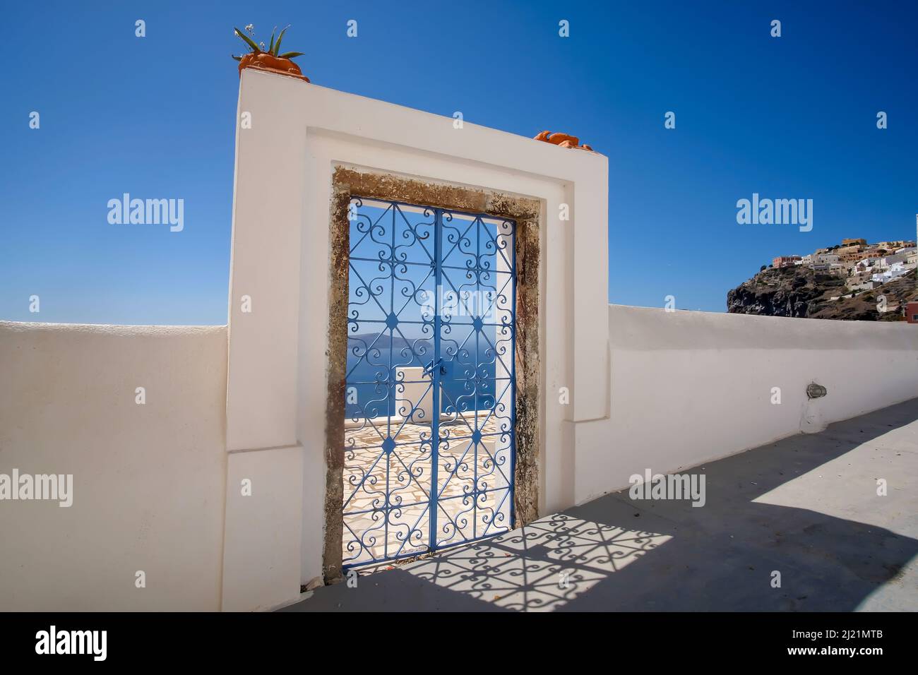 An external decorated door with flower plants on the roof of a villa and view  of the Fira and the  aegean sea in  Santorini Stock Photo