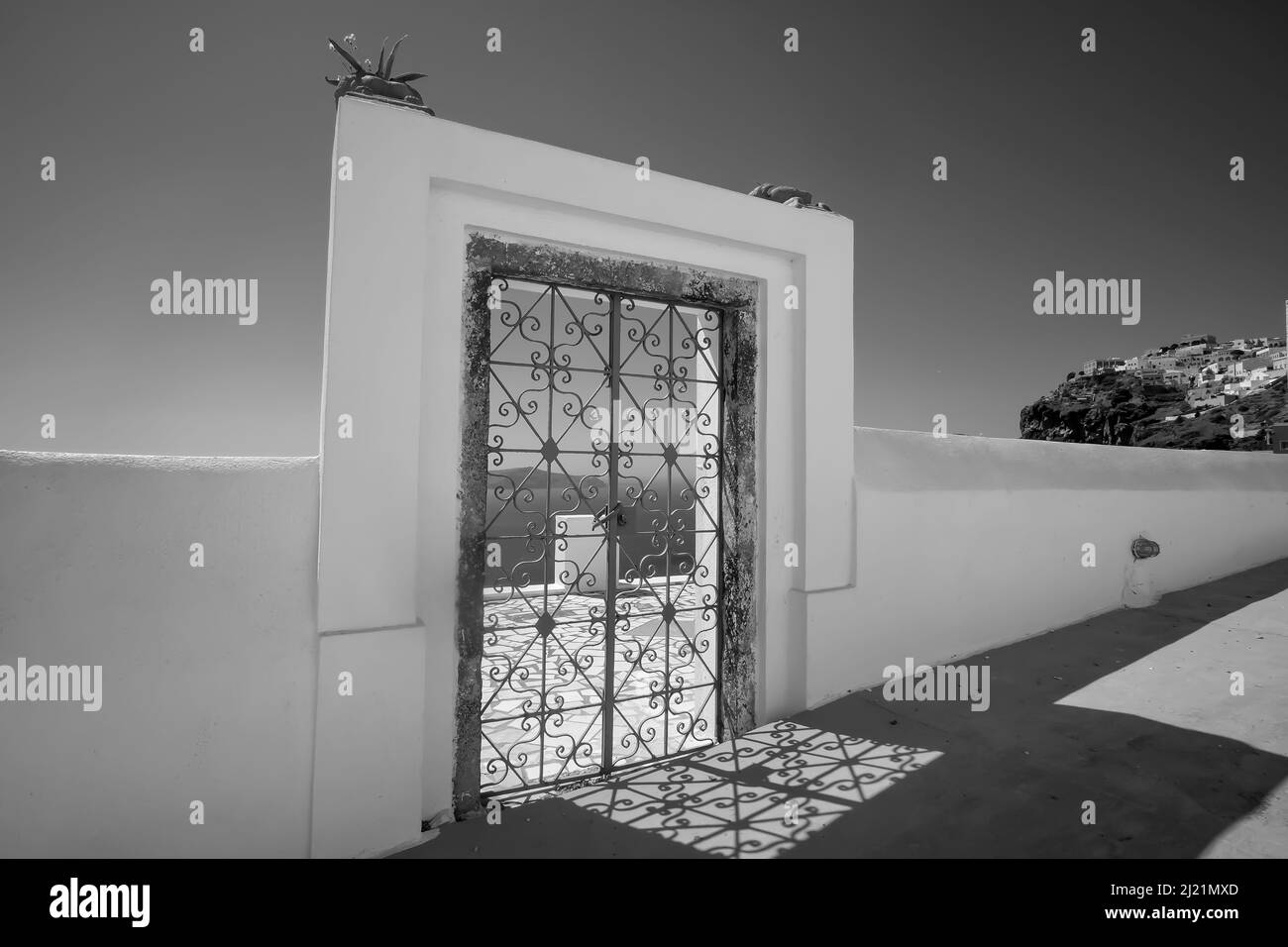 An external decorated door with flower plants on the roof of a villa and view  of the Fira and the  aegean sea in  Santorini in black and white Stock Photo