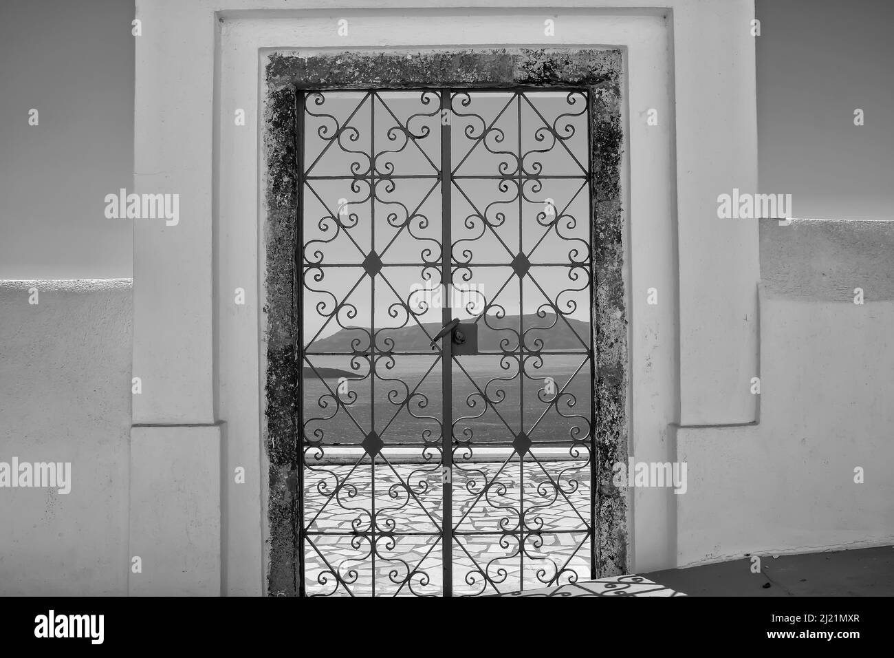 An external decorated door with flower plants on the roof of a villa and  view of the aegean sea in Fira Santorini in black and white Stock Photo