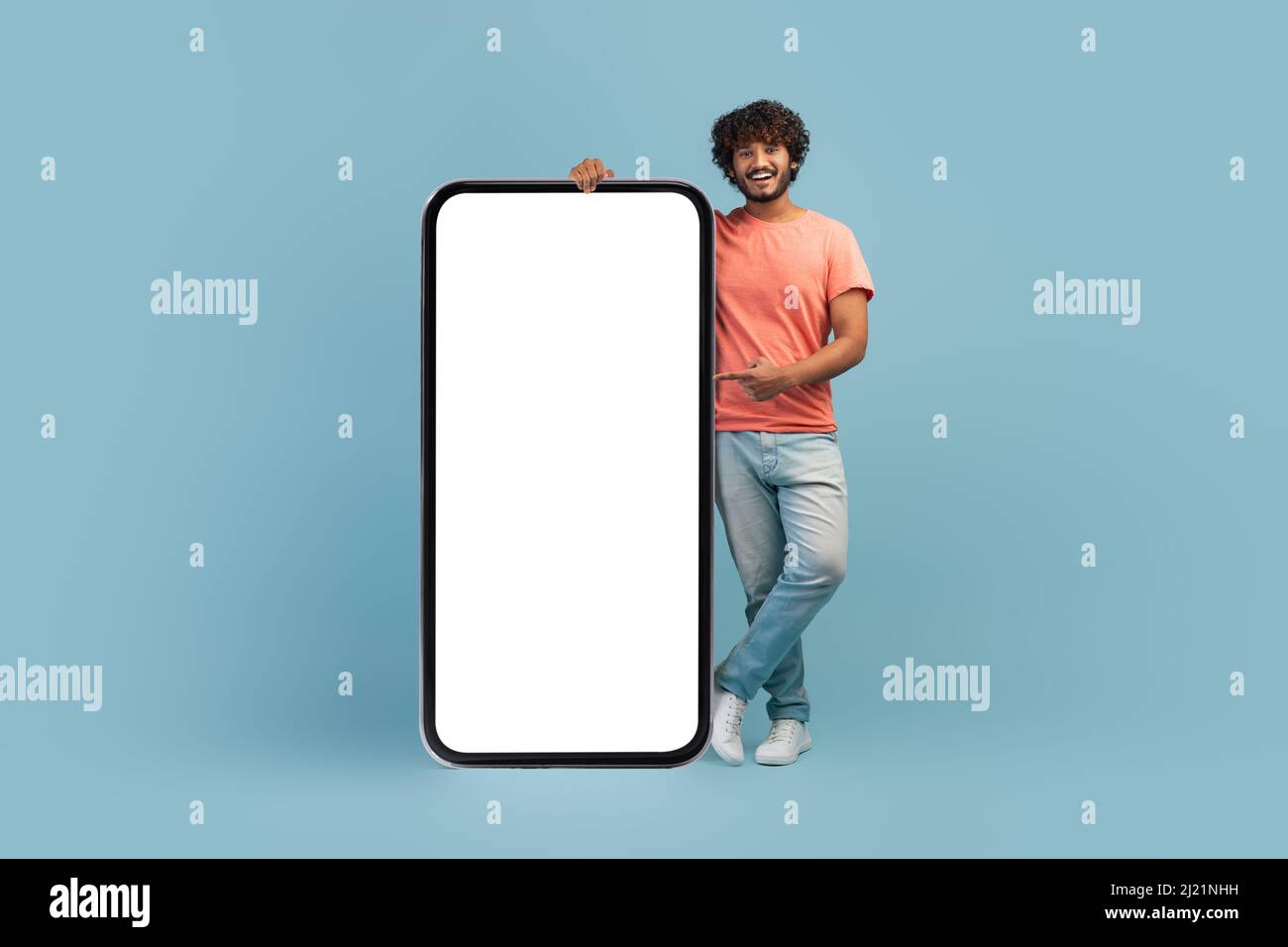 Stylish indian guy posing by huge smartphone with blank screen Stock Photo