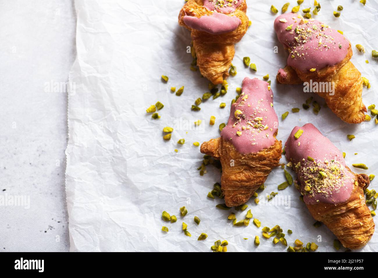 Mini-croissants with ruby chocolate and pistachios on a baking paper, gray background. Top view and copy space. Stock Photo