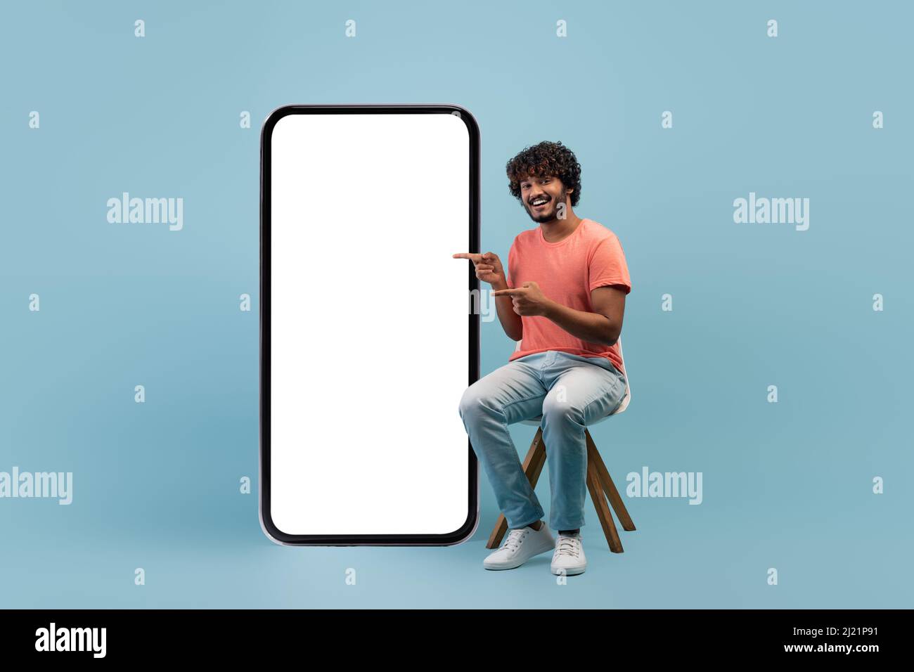 Positive indian guy in casual sitting by huge cell phone Stock Photo