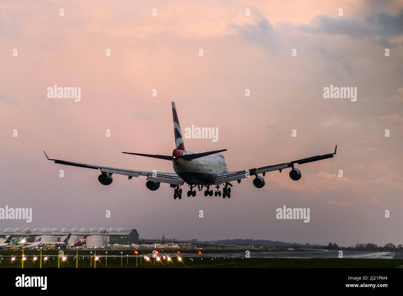 British Airways Boeing 747 -400 Jumbo Jet plane landing at London Heathrow Airport, UK, at dusk with sunset colours in cloudy sky. Runway lights Stock Photo