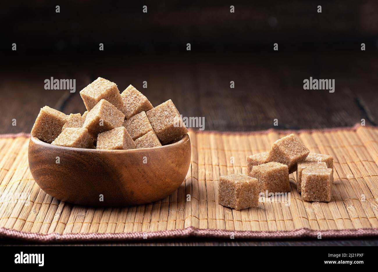 Refined cane sugar cubes in a wooden bowl on a mat. Copy space Stock
