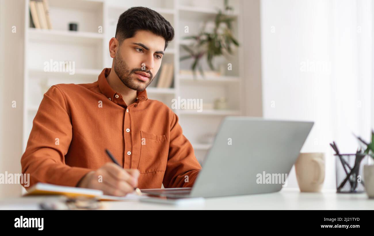 Portrait of focused Arab man using laptop and writing Stock Photo